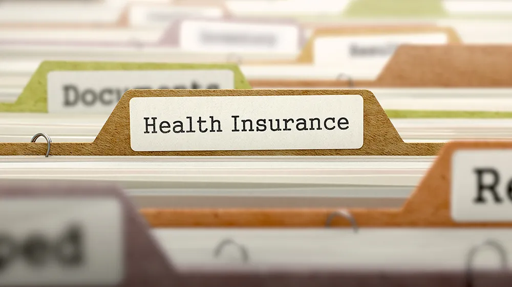 a bunch of stacked file folders with one labeled Health Insurance in the front