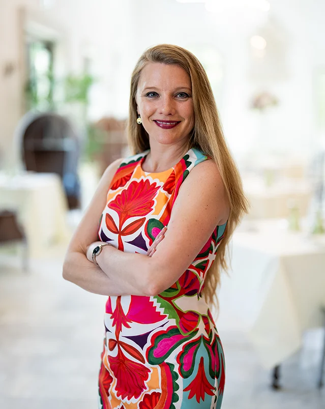 picture of a woman in brightly floral dress with arms crossed, smiling