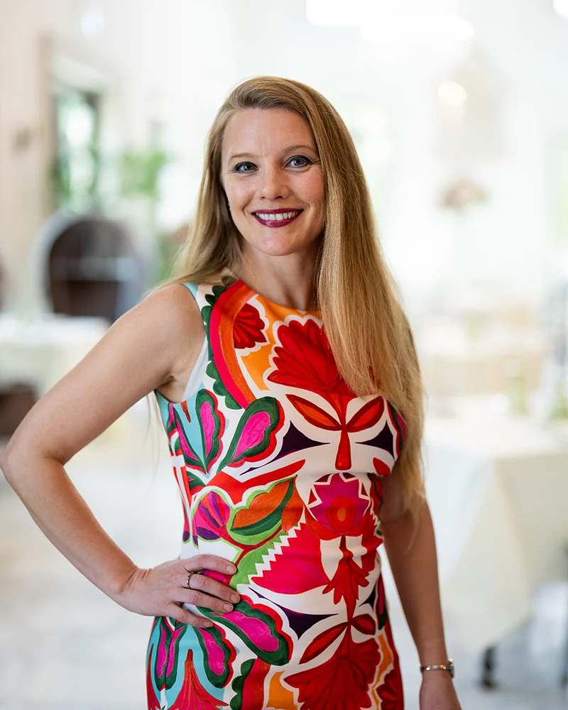 picture of a woman in brightly floral dress with hand on hip, smiling